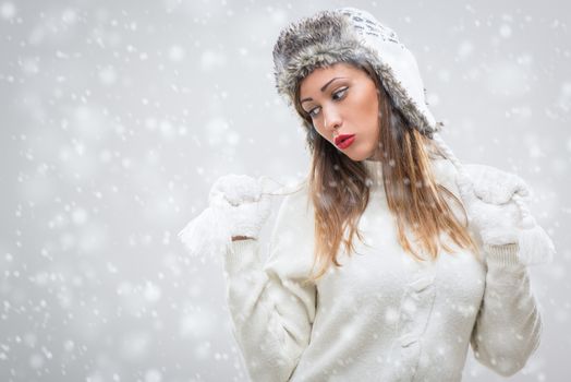 Beautiful young woman in warm clothing thinking while snowing.