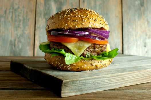 Gourmet burger with melted cheese, tomato and onion filling on top of a wooden chopping board