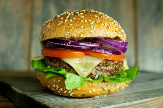 Cheese burger with tomato and onion filling on top of a wooden chopping board