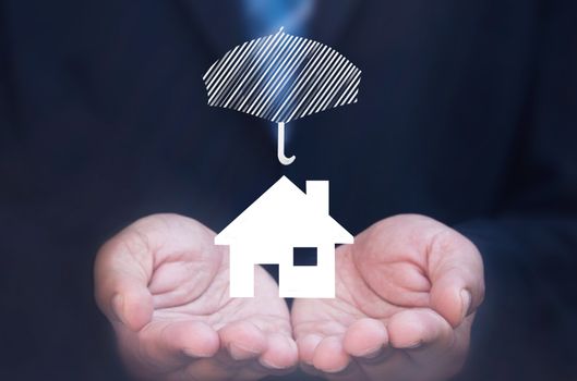 Business man holding a house icon protected by an umbrella 