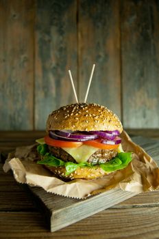 Rustic burger with melted cheese, tomato and onion filling on top of a wooden chopping board