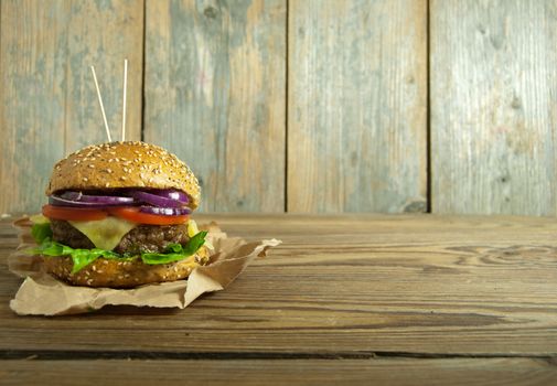 Gourmet burger with melted cheese, tomato and onion filling on top of a wooden chopping board