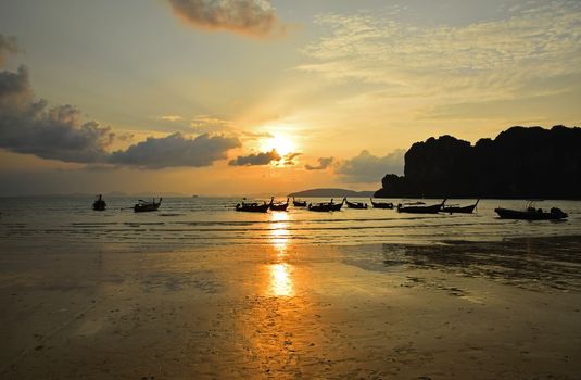 Traditional Thailand long tail boats silhouettes in water near beach during sunset in back light