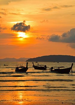 Traditional Thailand long tail boats silhouettes in water near beach during sunset in back light