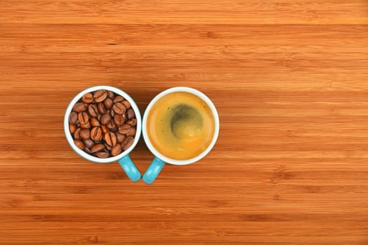 Two blue coffee cups of espresso and roasted Arabica beans over wooden bamboo board background