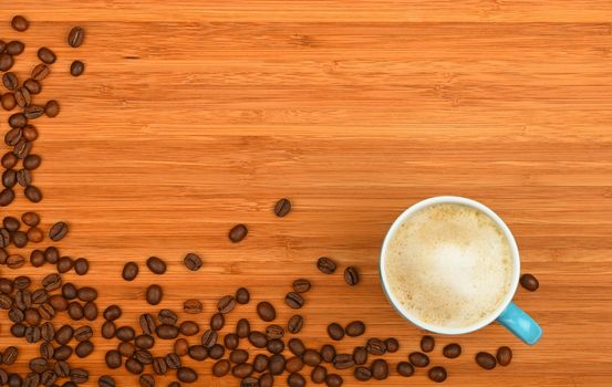 Blue coffee cup of latte cappuccino and roasted Arabica beans corner border shaped over wooden bamboo board background