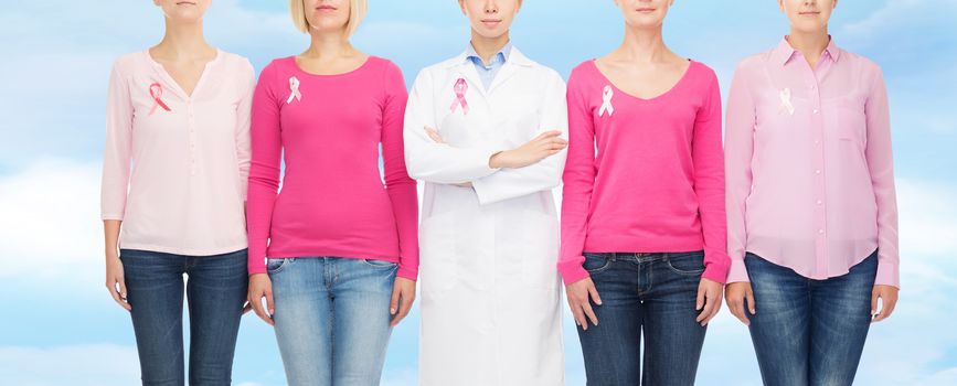 healthcare, people and medicine concept - close up of women in blank shirts with pink breast cancer awareness ribbons over blue sky background