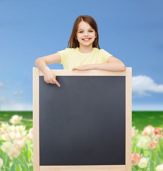 people, advertisement and education concept - happy little girl pointing finger to blackboard