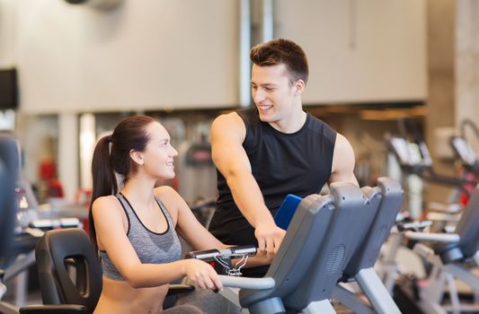 sport, fitness, lifestyle, technology and people concept - happy woman with trainer working out on exercise bike in gym