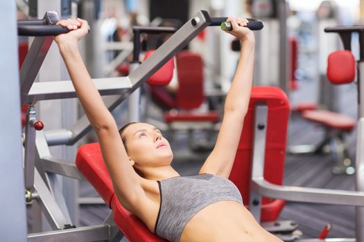 sport, fitness, lifestyle and people concept - young woman flexing muscles on gym machine