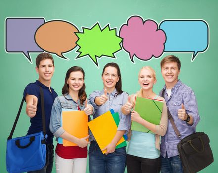 school, education, communication and people concept - group of smiling teenagers with folders and school bags showing thumbs up over green board background with text bubbles