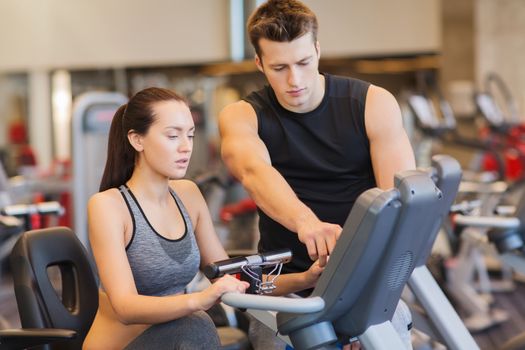 sport, fitness, lifestyle, technology and people concept - woman with trainer working out on exercise bike in gym