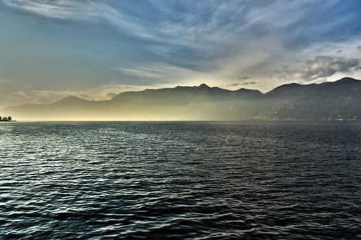 sunset over the lake major with the mists of the horizon and mountains in the background on a winter afternoon, Luino - Lombardy, Italy