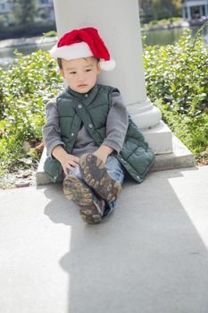 Melancholy Mixed Race Boy Sitting At The Park Wearing Christmas Santa Hat.