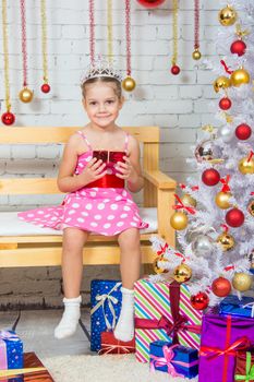Four-year girl sitting on a bench with a small gift from snowy Christmas trees
