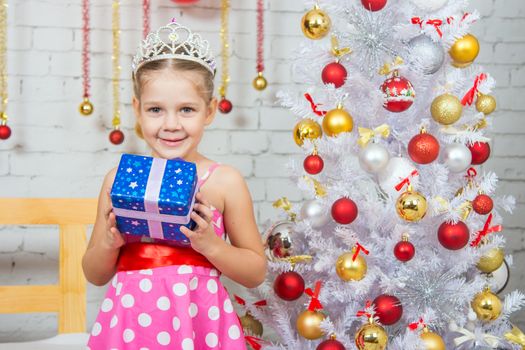 Four-year girl stands at the shops with a small gift from snowy Christmas trees