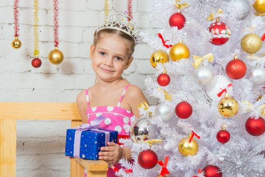 Four-year girl stands at the shops with a small gift from snowy Christmas trees