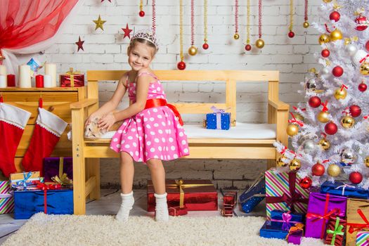 Cheerful girl four years stroking a cat sitting on a bench in the home New Years interior