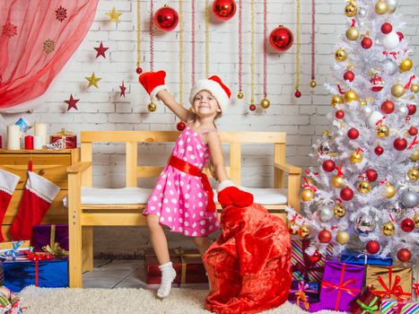 Cheerful little girl playing and having fun with a bag of gifts in the home New Years interior