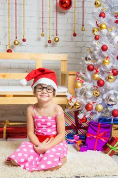 Girl in the red hat and the funny round glasses sits on a rug in the room with New Years interior