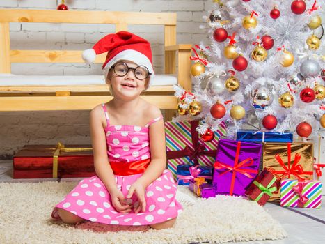 Girl in the red hat and the funny round glasses sits on a rug in the room with New Years interior