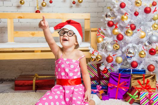 Girl in the red hat and the funny round glasses sits on a rug in the room with New Years interior