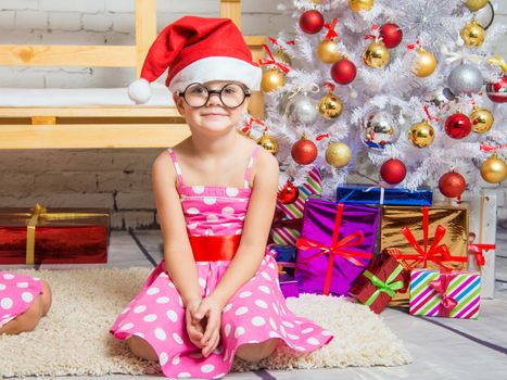 Girl in the red hat and the funny round glasses sits on a rug in the room with New Years interior