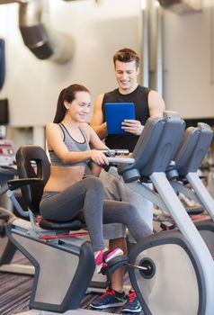 sport, fitness, lifestyle, technology and people concept - happy woman with trainer working out on exercise bike in gym