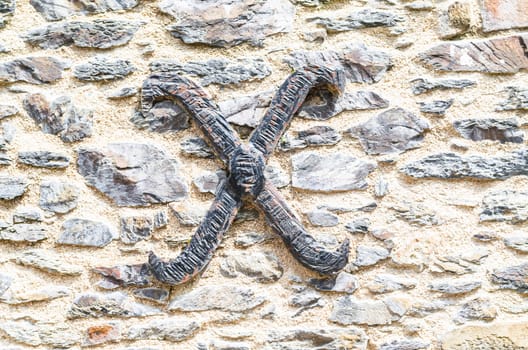 Old castle stone wall with the letter X made of wrought iron. texture background.