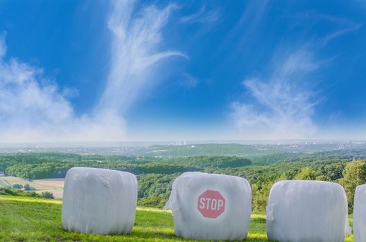 Three straw bales in white plastic film on a field. The average bale imprinted Stop.