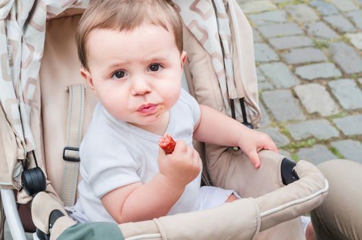 Little boy sitting in a stroller. Child holding a sausage in his hand