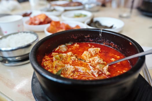 Korean spicy soup with tofu in a hot pot and a set of korean snacks ("banchan") on background with selected focus 