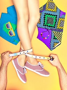 Fashion clothes stylish set, accessories, womans sexy legs, people. Hipster girl creative look in trendy gumshoes, top, shorts, sunglasses. Mans hands holding belt. Vivid youth style, yellow,copyspace