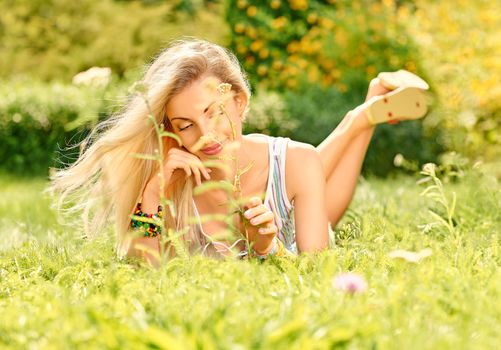 Beauty playful woman relax in summer garden dreaming on grass, people, outdoors, bokeh. Attractive happy blonde girl enjoying nature, harmony on meadow, lifestyle.Sunny day, forest, flowers, copyspace