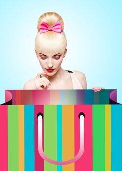 Fashion beauty portrait of woman with huge shopping bag waiting for presents on blue background, people, copyspace. Confident blonde girl with Pinup hairstyle, fringe and pink bow. Billboard