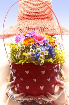 Woman with basket of wildflowers in hands. Young blonde boho girl in orange hat on summer meadow, people. Attractive joyfull, romantic style, floral sundress. Sunny day