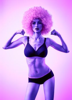 Beauty fashion. Fitness woman, unusual look. Sexy athletic body, people. Provocative attractive girl posing in trendy sport bra, shorts with afro hairstyle, purple background, copyspace, toned