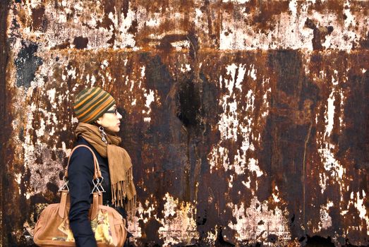 beautiful young adult woman in a cap and glasses  against a grungy rusty  wall