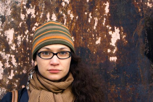 beautiful young adult woman in a cap and glasses  against a grungy rusty  wall