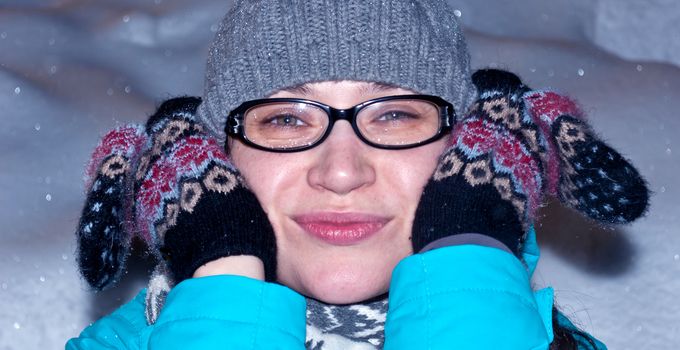 The happy girl in a cap and glasses clasps a head hands in gloves