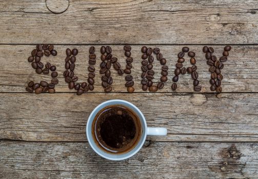 Cup of coffee on wooden background and SUNDAY coffee beans 