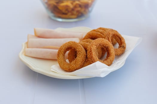 Close up detailed front view of a plate of fried onion rings with jambon served on a plate.