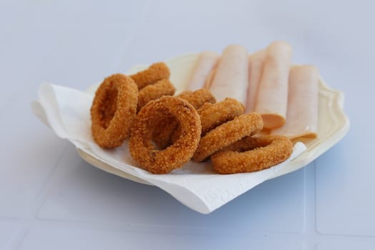 Close up detailed front view of a plate of fried onion rings with jambon served on a plate.