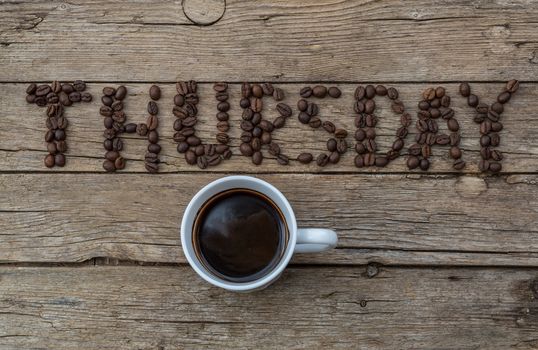 Cup of coffee on wooden background and THURSDAY coffee beans 