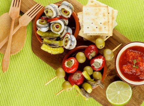 Delicious Spanish Snacks with Green Olives, Stuffed Small Peppers,Tomatoes Sauce, Anchovies in Various Bowls with Bread Sticks and Wooden Forks closeup on Green Napkin. Top View