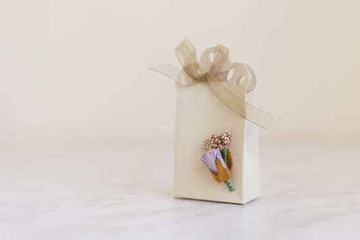 Close up detailed front view of hand-crafted white gift box with small flowers and colorful ribbons.