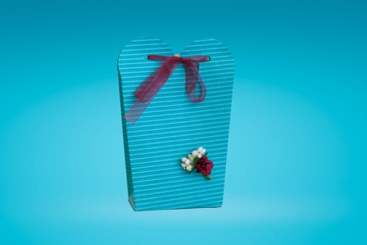 Close up detailed front view of hand-crafted green gift box with small flowers and colorful ribbons, on green background.