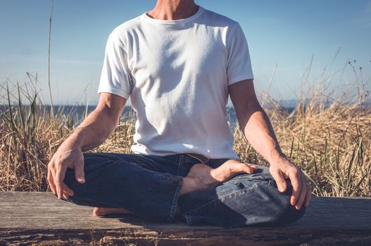 Man sitting in a relaxed yoga pose at the beach.