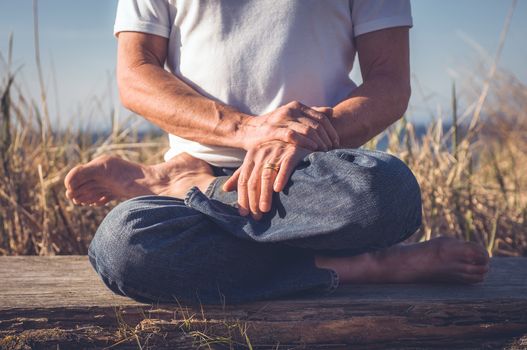 Man sitting in a relaxed yoga pose at the beach.