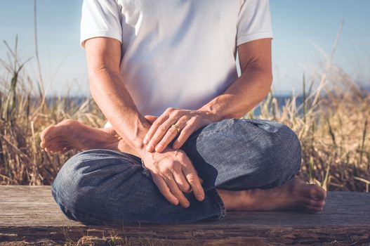 Man sitting in a relaxed yoga pose at the beach.